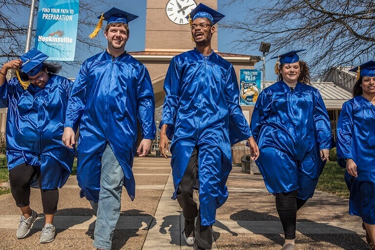 graduates walking in caps and gowns on campus
