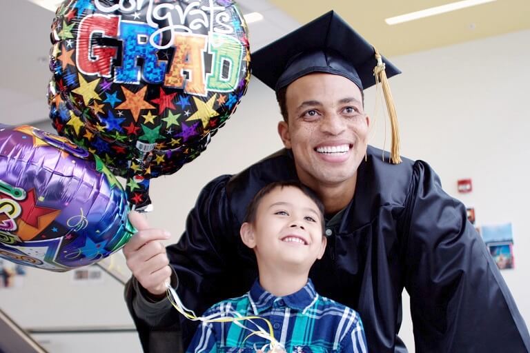 Male graduate holding balloons with little boy