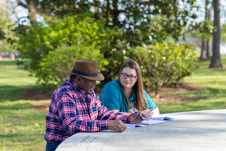 Brittanie Bogard talking with another students while sitting at a table outside. 